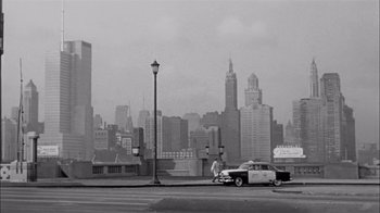 Movie still from “The Harder They Fall” (1956), directed by Mark Robson – An old truck parked on the side of the road in front of a city skyline; Extreme Wide shot, High angle