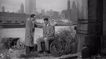 Movie still from “The Harder They Fall” (1956), directed by Mark Robson – Two men are sitting on a bench near a body of water; Wide shot, High angle