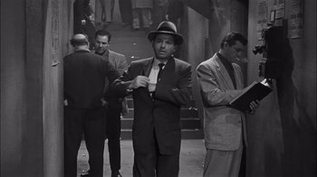 Movie still from “The Harder They Fall” (1956), directed by Mark Robson – Black and white photograph of a man in a suit and hat; Medium shot, High angle