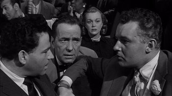 Movie still from “The Harder They Fall” (1956), directed by Mark Robson – A black and white photo of a group of men and a woman; Close Up shot, Over the shoulder angle