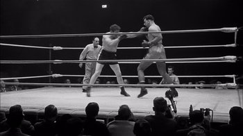 Movie still from “The Harder They Fall” (1956), directed by Mark Robson – Two men in a boxing ring fighting in front of a crowd of onlookers; Wide shot, Low angle