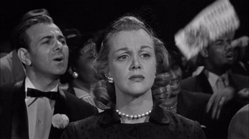 Movie still from “The Harder They Fall” (1956), directed by Mark Robson – A woman in a crowd of people wearing pearls; Medium shot, Low angle