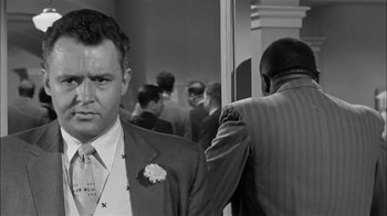 Movie still from “The Harder They Fall” (1956), directed by Mark Robson – Black and white photograph of a man in a suit and tie next to another man in a suit and tie; Close Up shot, Over the shoulder angle