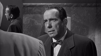 Movie still from “The Harder They Fall” (1956), directed by Mark Robson – A man in a suit and bow tie looking at the camera; Close Up shot, Over the shoulder angle