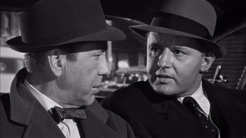 Movie still from “The Harder They Fall” (1956), directed by Mark Robson – A black and white photo of two men in hats; Close Up shot, Over the shoulder angle