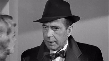 Movie still from “The Harder They Fall” (1956), directed by Mark Robson – An older man wearing a hat and bow tie; Close Up shot, Over the shoulder angle