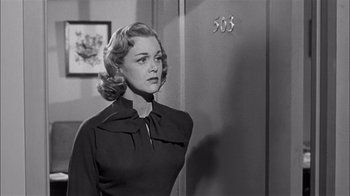 Movie still from “The Harder They Fall” (1956), directed by Mark Robson – A black and white photo of a woman standing in front of a door; Medium shot, Low angle