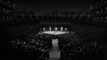 Movie still from “The Harder They Fall” (1956), directed by Mark Robson – A boxing match in an arena with a crowd watching; Extreme Wide shot, High angle