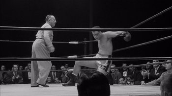 Movie still from “The Harder They Fall” (1956), directed by Mark Robson – An old photo of a man in a boxing ring; Wide shot, Low angle