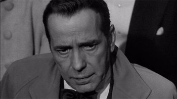 Movie still from “The Harder They Fall” (1956), directed by Mark Robson – An old black and white photo of a man in a suit and bow tie; Close Up shot, Over the shoulder angle