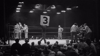 Movie still from “The Harder They Fall” (1956), directed by Mark Robson – A man holding up a sign in front of a crowd; Extreme Wide shot, High angle