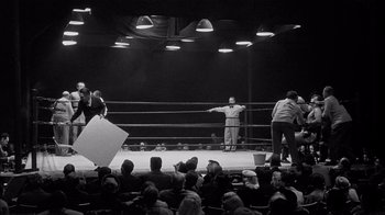 Movie still from “The Harder They Fall” (1956), directed by Mark Robson – A boxing match in progress in an arena with spectators watching; Extreme Wide shot, High angle