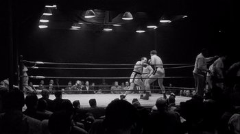 Movie still from “The Harder They Fall” (1956), directed by Mark Robson – A boxing match in a boxing ring with spectators watching; Extreme Wide shot, High angle