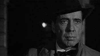 Movie still from “The Harder They Fall” (1956), directed by Mark Robson – Black and white photograph of a man wearing a hat and bow tie; Close Up shot, Over the shoulder angle