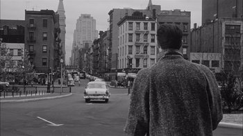 Movie still from “The Harder They Fall” (1956), directed by Mark Robson – A man standing on the side of a road in the middle of a city; Wide shot, High angle