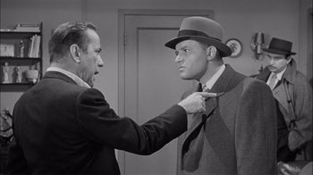 Movie still from “The Harder They Fall” (1956), directed by Mark Robson – An older man and a younger man in a suit and tie; Medium shot, Over the shoulder angle