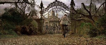 Movie still from “The Haunted Mansion” (2003), directed by Rob Minkoff – A person riding a bike in front of an iron gate; Extreme Wide shot, Low angle