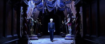 Movie still from “The Haunted Mansion” (2003), directed by Rob Minkoff – A man in a suit stands in front of statues; Wide shot, Low angle