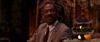 Movie still from “The Haunted Mansion” (2003), directed by Rob Minkoff – A man in a suit and tie sitting in front of an ornate chair; Close Up shot, Low angle
