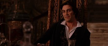 Movie still from “The Haunted Mansion” (2003), directed by Rob Minkoff – A man sitting in front of a wooden wall holding a glass; Medium shot, Low angle