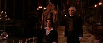 Movie still from “The Haunted Mansion” (2003), directed by Rob Minkoff – A man sitting in front of another man in front of a wooden chair; Medium shot, Low angle