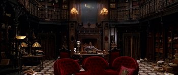 Movie still from “The Haunted Mansion” (2003), directed by Rob Minkoff – A man sitting at a desk in front of a fireplace; Wide shot, High angle