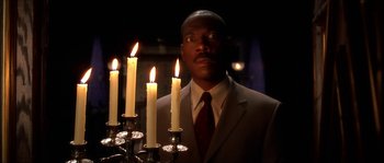 Movie still from “The Haunted Mansion” (2003), directed by Rob Minkoff – A man standing in front of a bunch of lit candles; Medium shot, Low angle