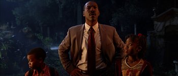 Movie still from “The Haunted Mansion” (2003), directed by Rob Minkoff – A man in a suit and tie standing in front of trees; Medium shot, Low angle