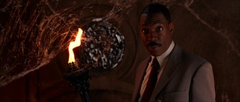 Movie still from “The Haunted Mansion” (2003), directed by Rob Minkoff – A man standing next to a lit fire; Medium shot, Low angle