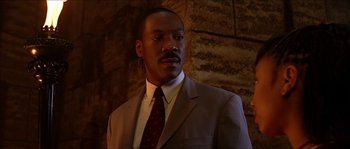 Movie still from “The Haunted Mansion” (2003), directed by Rob Minkoff – A man wearing a suit and tie standing in front of a brick wall; Close Up shot, Low angle