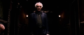 Movie still from “The Haunted Mansion” (2003), directed by Rob Minkoff – An old man in a suit standing in a dark room; Medium shot, Low angle
