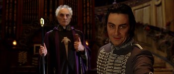 Movie still from “The Haunted Mansion” (2003), directed by Rob Minkoff – A man in a purple robe stands next to another man in a black robe; Medium shot, Over the shoulder angle