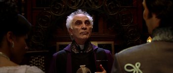 Movie still from “The Haunted Mansion” (2003), directed by Rob Minkoff – An older man in a priest's outfit is holding a microphone; Close Up shot, Low angle