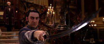 Movie still from “The Haunted Mansion” (2003), directed by Rob Minkoff – A man holding a sword in a room with candles in the background; Medium shot, Low angle