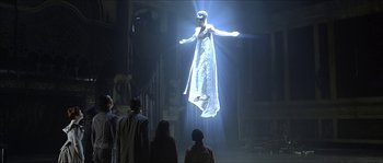 Movie still from “The Haunted Mansion” (2003), directed by Rob Minkoff – A group of people standing around watching an image projected on a wall; Wide shot, Low angle