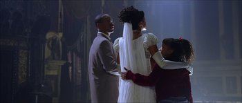 Movie still from “The Haunted Mansion” (2003), directed by Rob Minkoff – A man and a woman standing next to each other in front of another man; Medium shot, Over the shoulder angle