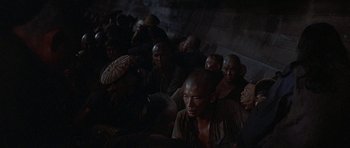 Movie still from “The Hawaiians” (1970), directed by Tom Gries – A group of people sitting in a dark room; Wide shot, High angle