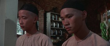 Movie still from “The Hawaiians” (1970), directed by Tom Gries – Two asian men wearing black hats in front of a brick wall; Close Up shot, Low angle