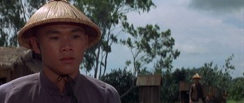 Movie still from “The Hawaiians” (1970), directed by Tom Gries – A man wearing a straw hat standing in front of trees; Close Up shot, Low angle