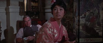 Movie still from “The Hawaiians” (1970), directed by Tom Gries – A woman in a pink kimono sitting next to a man in a suit; Medium shot, Over the shoulder angle