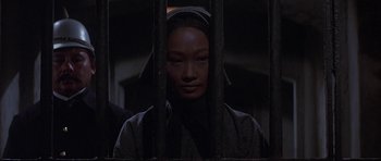 Movie still from “The Hawaiians” (1970), directed by Tom Gries – A woman in a hooded jacket behind bars in a dark room; Close Up shot, Low angle