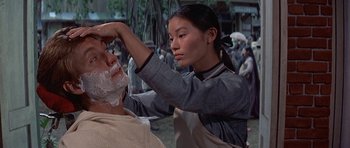 Movie still from “The Hawaiians” (1970), directed by Tom Gries – A woman is shaving a man's face in front of a crowd of onlookers; Close Up shot, Over the shoulder angle