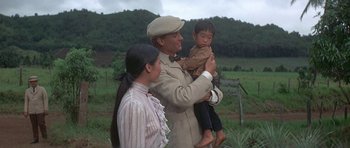 Movie still from “The Hawaiians” (1970), directed by Tom Gries – A man holding a young child while standing next to a woman; Medium shot, Low angle