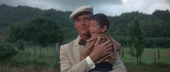 Movie still from “The Hawaiians” (1970), directed by Tom Gries – A man holding a young boy in his arms; Close Up shot, Low angle