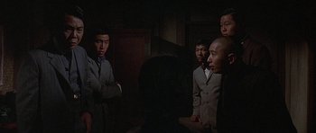 Movie still from “The Hawaiians” (1970), directed by Tom Gries – A group of men standing in a dark room; Medium shot, Over the shoulder angle