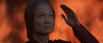 Movie still from “The Hawaiians” (1970), directed by Tom Gries – An asian woman is saluting in front of an orange background; Close Up shot, Low angle