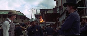 Movie still from “The Hawaiians” (1970), directed by Tom Gries – A man in a fireman's uniform standing in front of a burning building; Wide shot, Over the shoulder angle