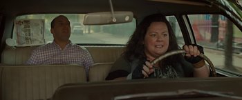 Movie still from “The Heat” (2013), directed by Paul Feig – A woman sitting in the back seat of a car while a man sits in the passenger seat; Medium shot, Over the shoulder angle