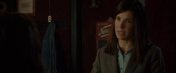 Movie still from “The Heat” (2013), directed by Paul Feig – A woman standing in a dark room with a person in the background; Close Up shot, Over the shoulder angle