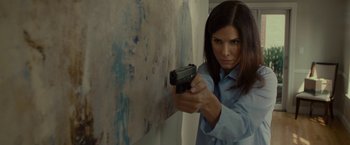 Movie still from “The Heat” (2013), directed by Paul Feig – A woman holding a gun in front of a wall; Medium shot, Low angle